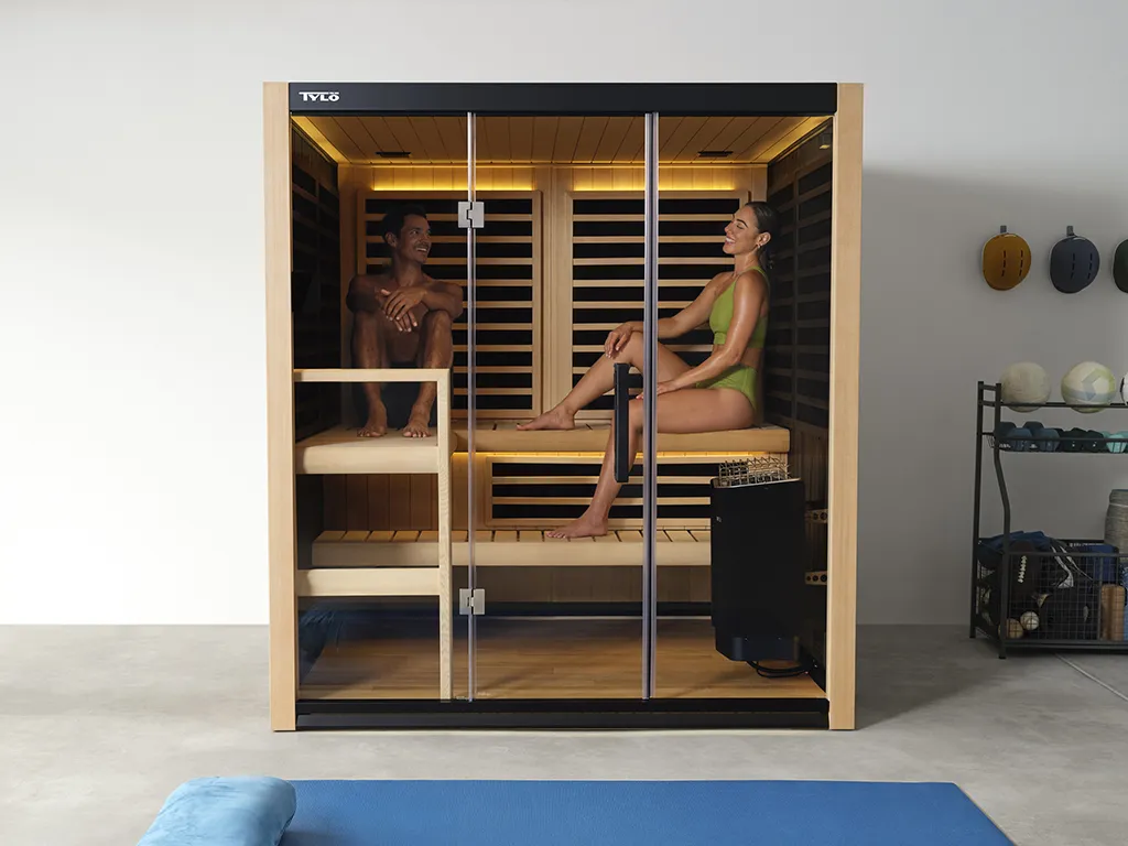 A zoomed out view of two people sitting inside of a Tylo Kiruna Hybrid sauna, relaxing and laughing