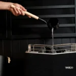 A person pouring water over a black Tylo sauna heater
