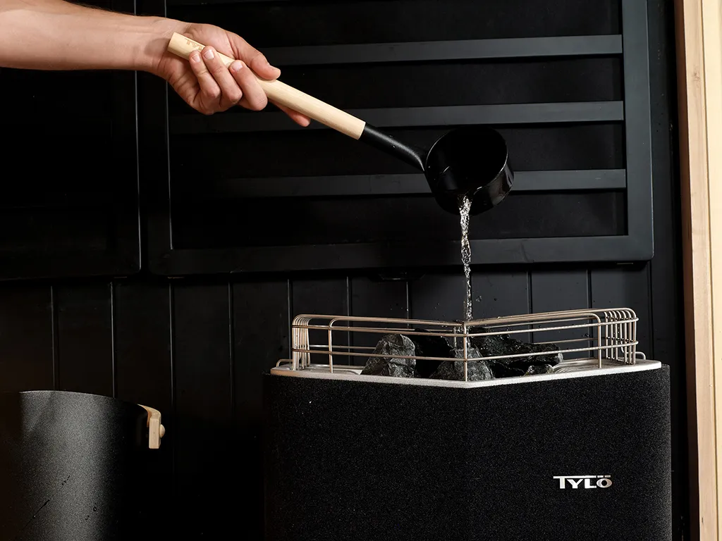 A person pouring water over a black Tylo sauna heater