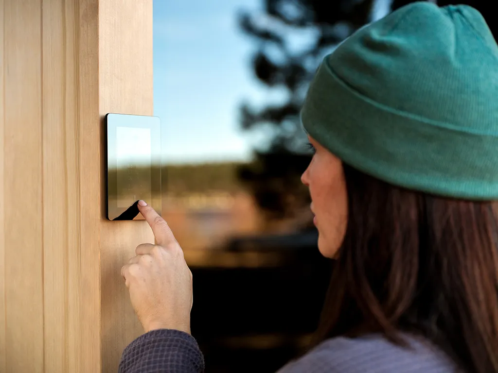 A person using a Tylo sauna digital feature outside of the sauna wearing a green hat
