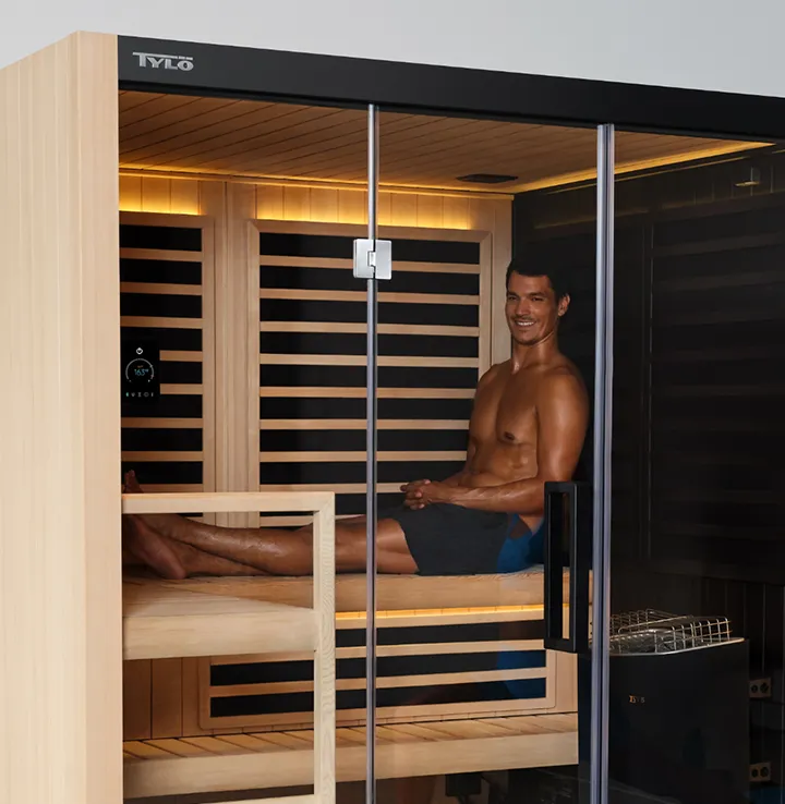A person sitting inside of a Tylo hybrid sauna smiling and relaxing